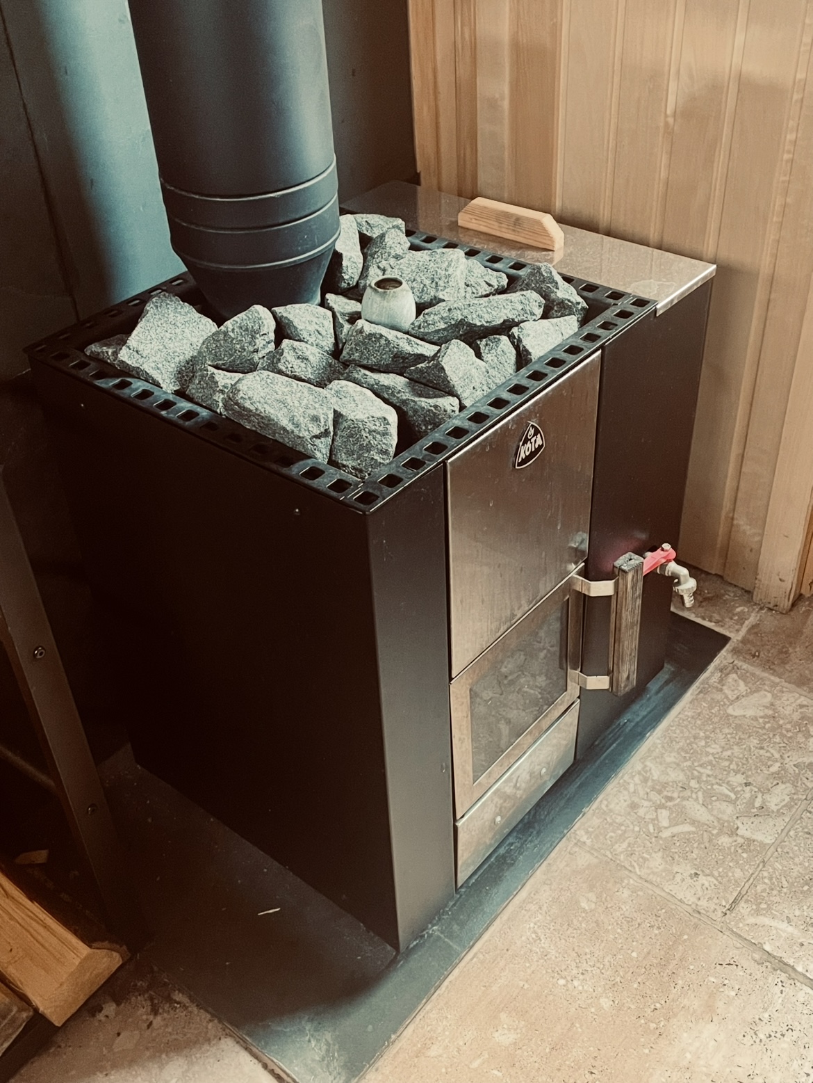 Wood-fired sauna stove with stones and travertine floor inside the Forma sauna